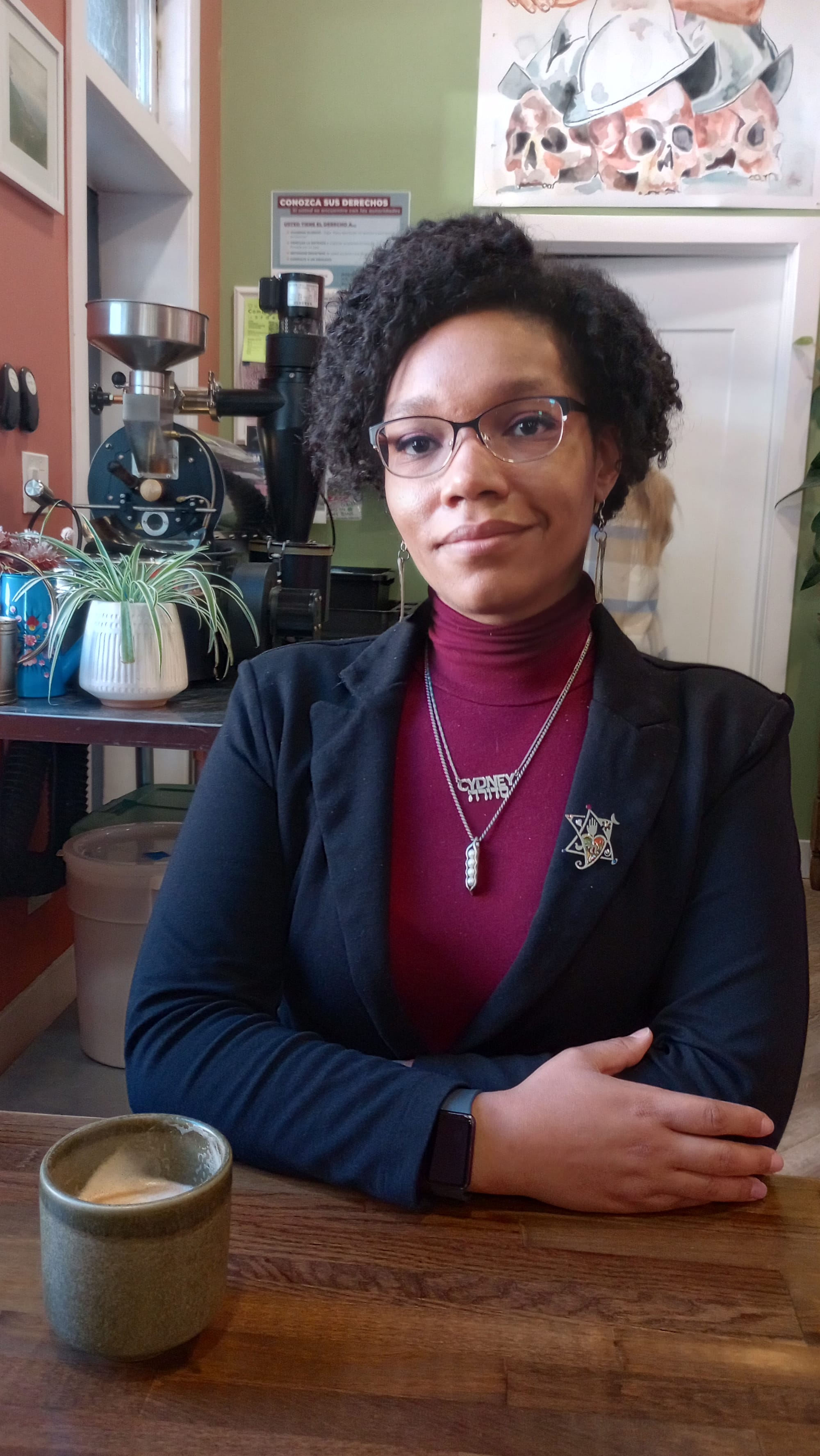 Portrait of Cydney Wallace, seated, with a coffee cup at her elbow.