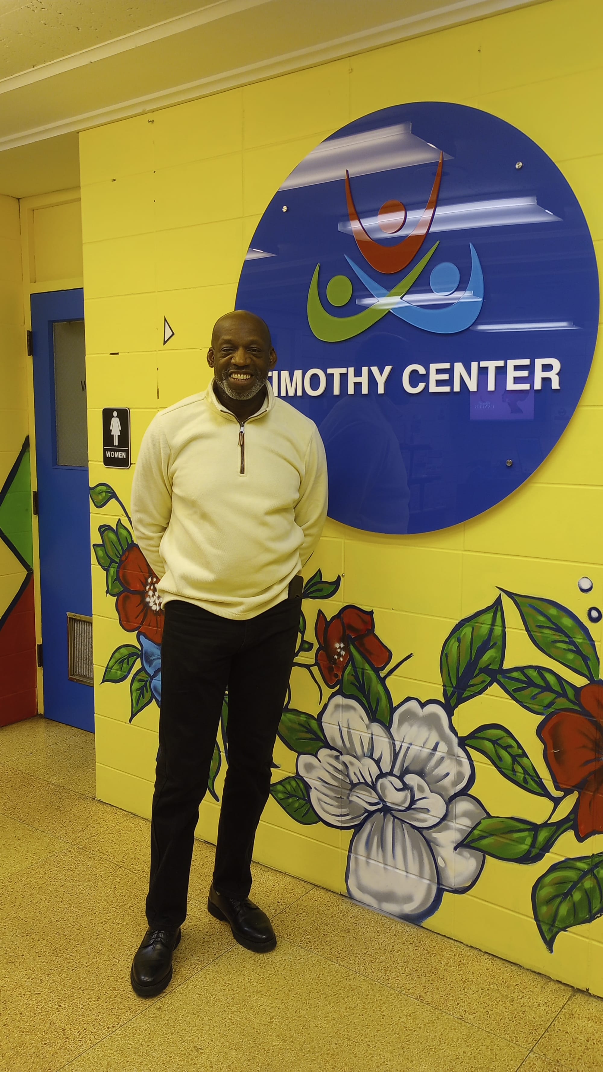 A man stands in front of a wall painted with a flower mural.