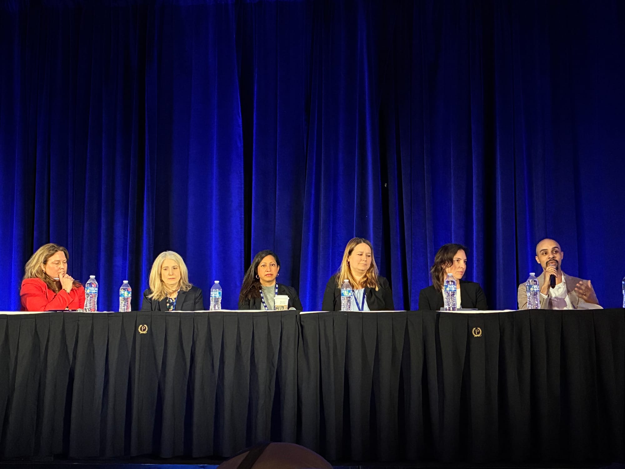 Six panelists sit at a long table.