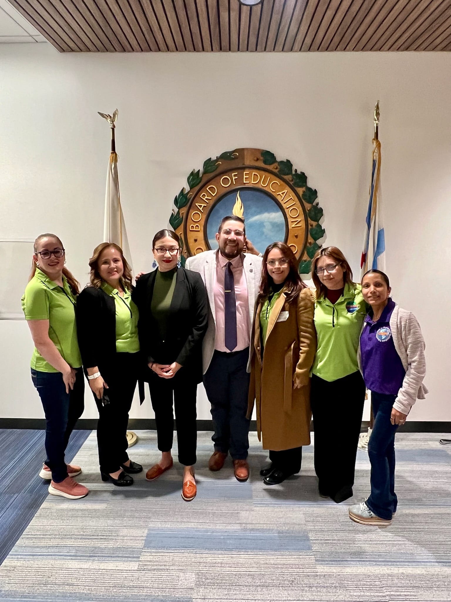 The photo shows a group of seven people posed by the Chicago Board of Education seal. In the center is board member Carlos Rivas. On his right is board member Yesenia Lopes. The other people are members of the Chicago Public Schools Multilingual Parent Council.