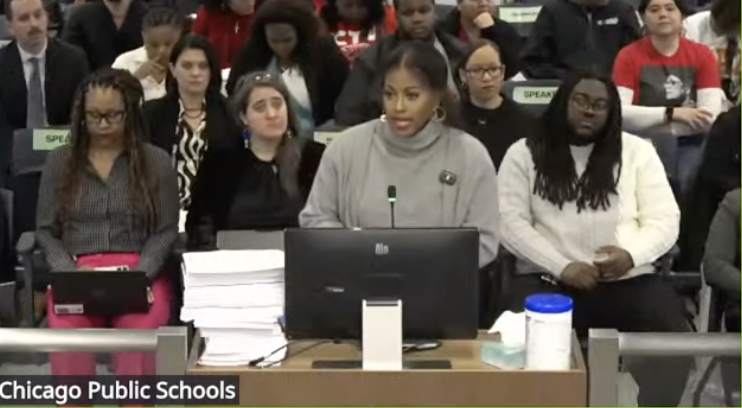 CTU President Stacy Davis Gates stands at a mic on a lectern, next to a large stack of white paper, with a crowd behind her.