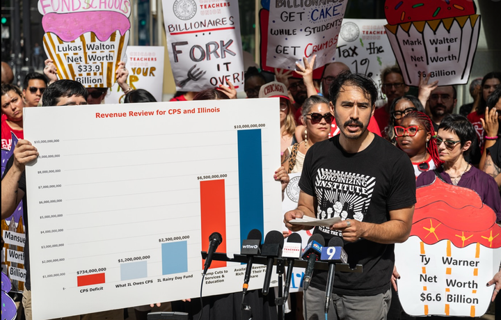 A man with a mustache explains a chart shows the Chicago Public Schools $734 millon deficit in comparison to potential revenue sources. context