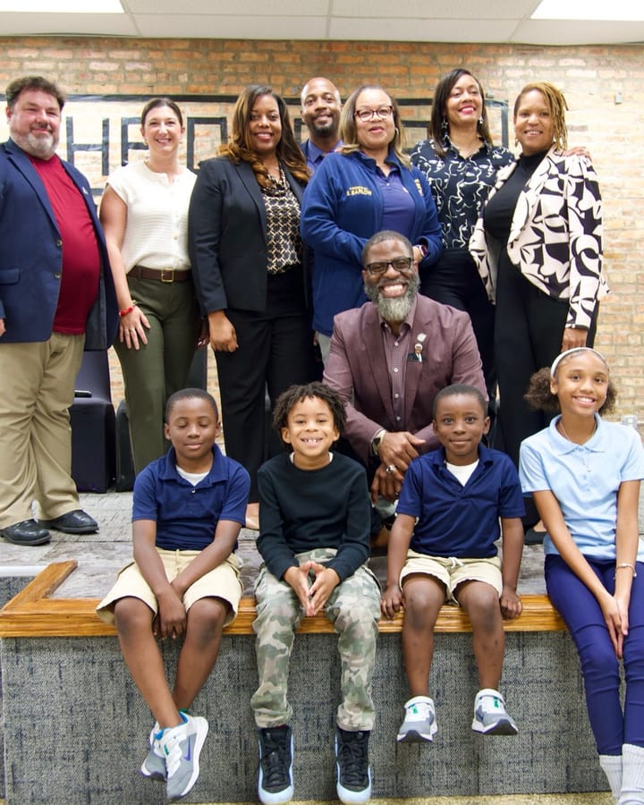 Board Member Che "Rhymefest" Smith sits in the center of a group photo with four young children in front.