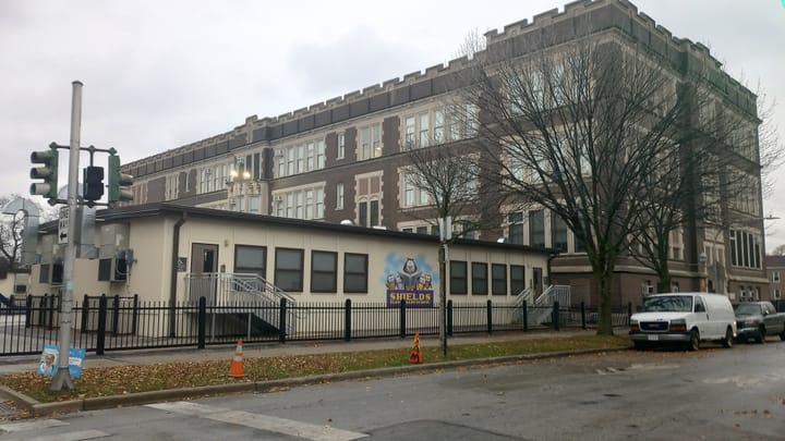 The photos shows the massive main building of Shields Elementary in the background, two modular classroom units in the foreground.