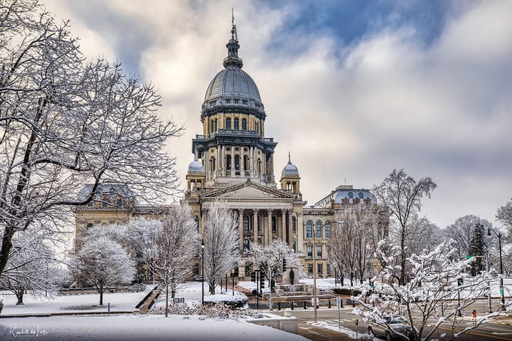 The photos shows the Illinois State Capitol, in Springfield,Illinois, in winter, with light snow on the ground and trees.